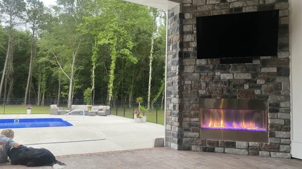 Outside stone fireplace under a covered patio open to the pool in the backyard